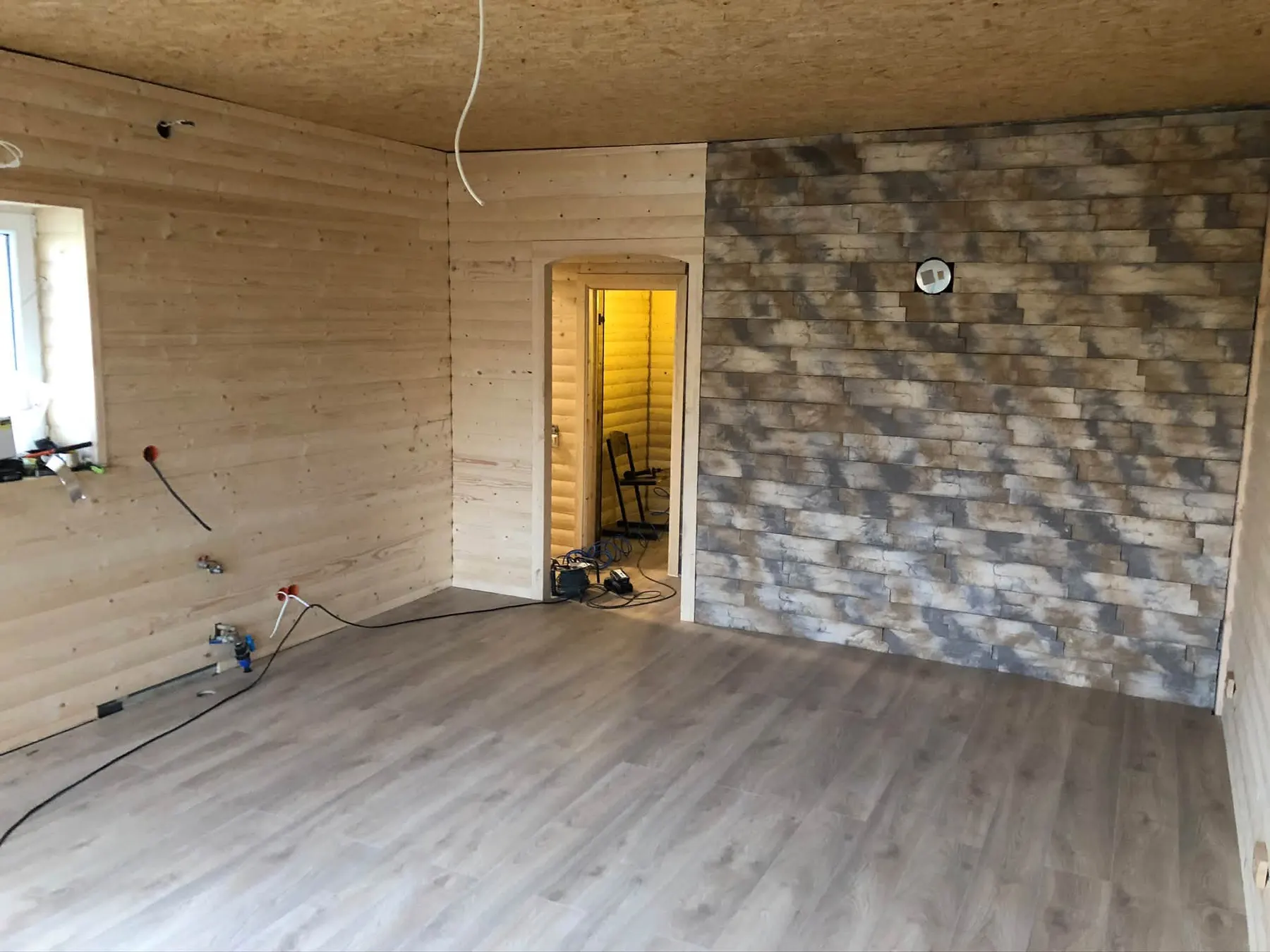 Istaba ar koka sienām, akmens imitācijas akcenta sienu un pelēku lamināta grīdu