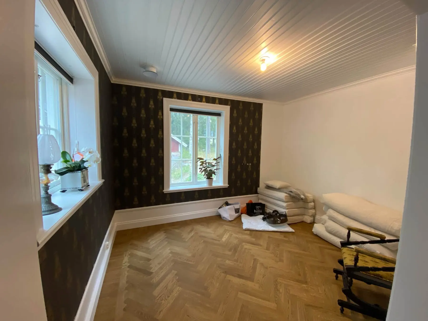 Istaba ar tumšām rakstainām tapetēm, baltiem logiem un eglītes parketu