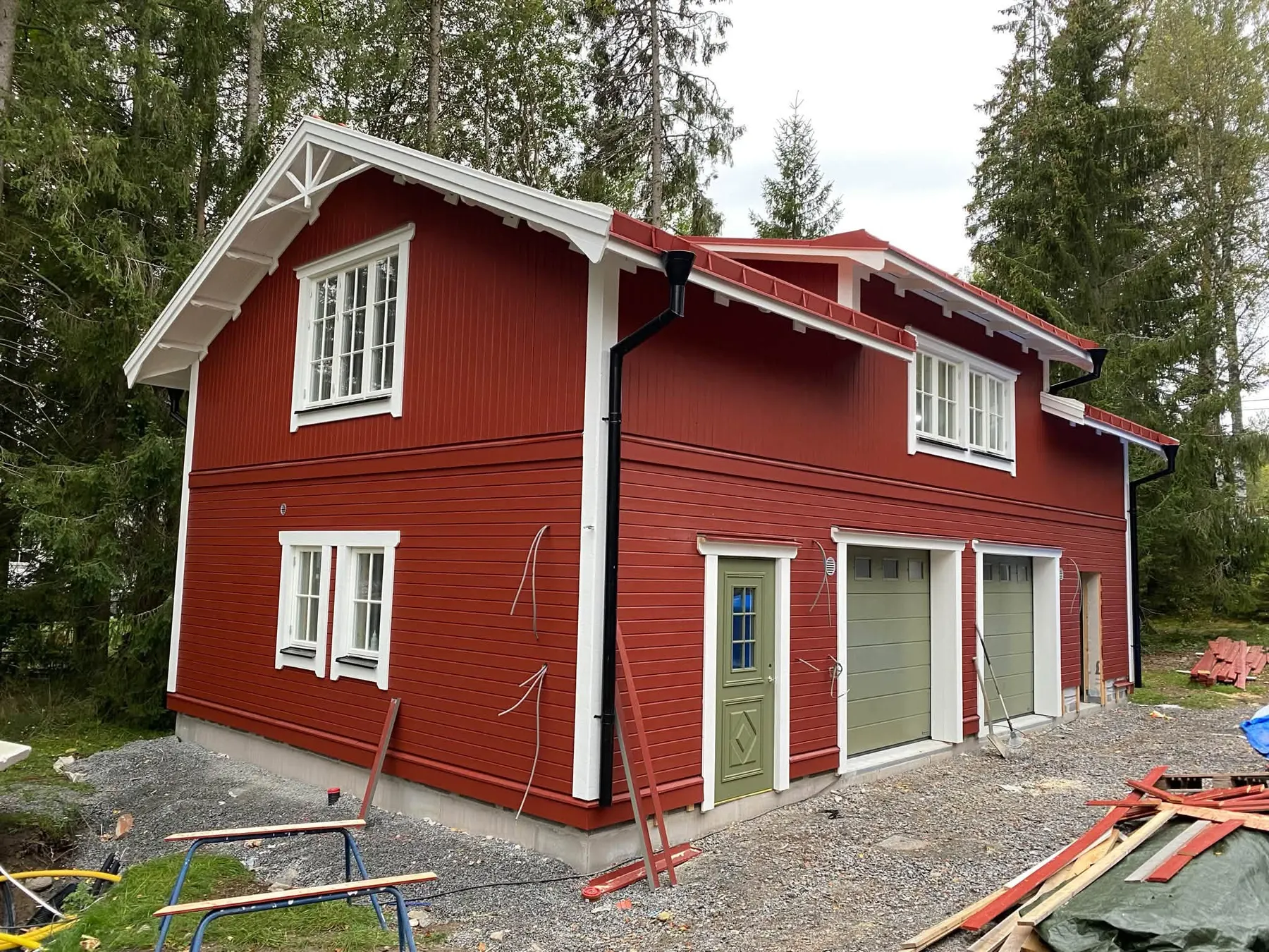 Sarkana divstāvu koka māja ar baltām apdarēm, verandu un divām garāžas durvīm